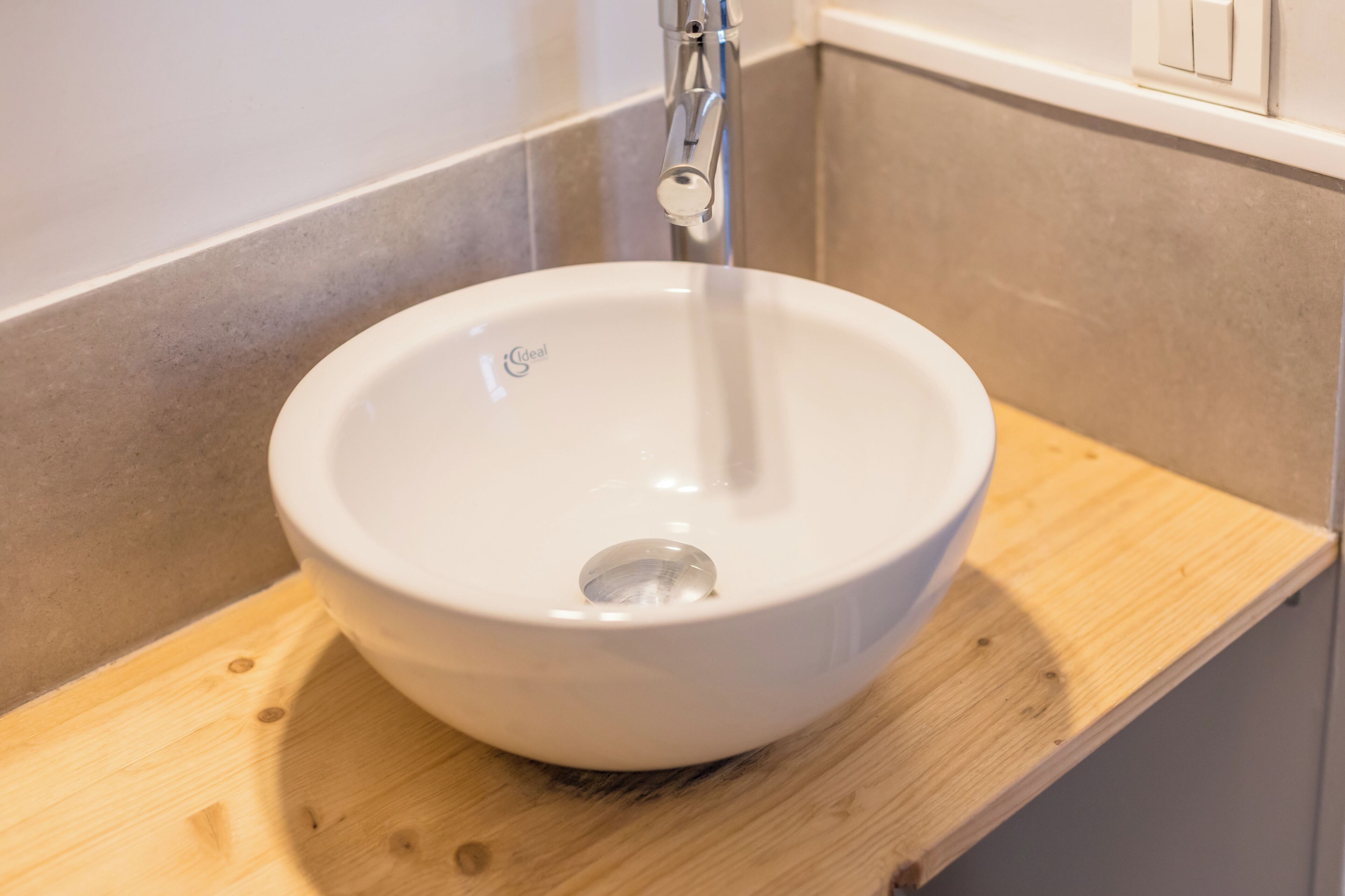 Un lavabo de cerámica blanca con un solo grifo sobre una repisa de madera en un baño.