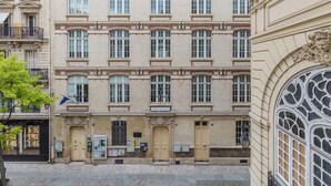 A multi-story building with a symmetrical facade, featuring evenly spaced windows, decorative moldings, and a central entrance with a door and a small balcony. - WS Louvre - Etienne Marcel (Paris)