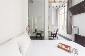 Quarto de hotel com uma cama grande, área de jantar com duas cadeiras, uma mesa e televisão presa na parede.