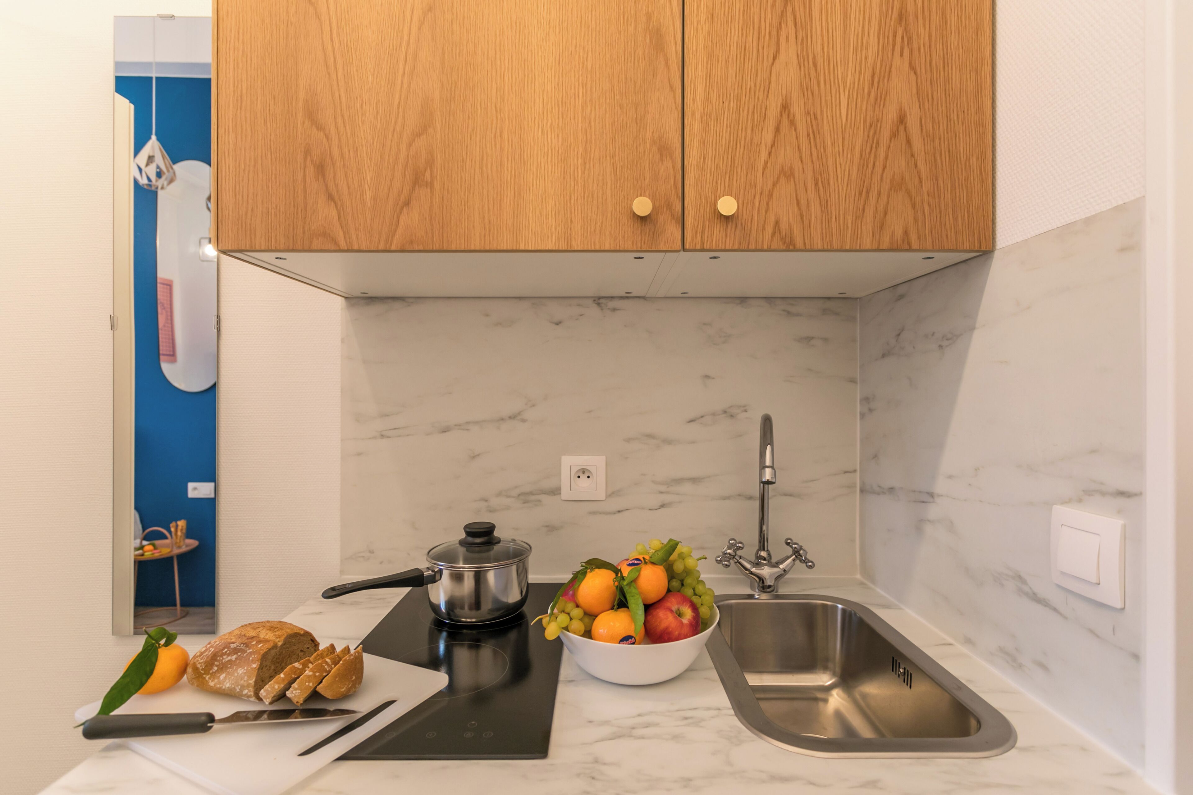 A modern kitchen with wooden cabinets, a marble backsplash, a sink, a stove, and a bowl of fruit.