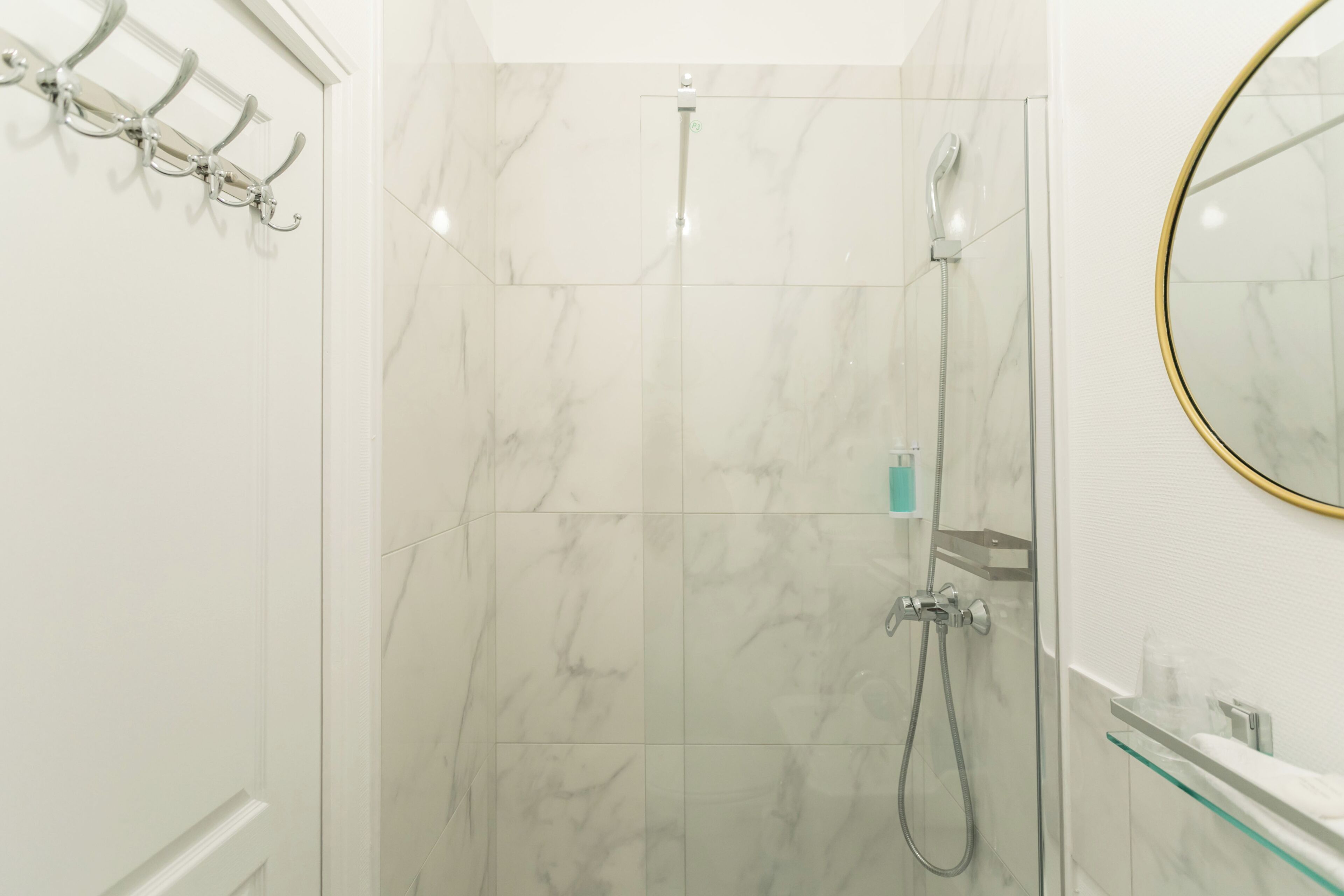 Une salle de bain moderne dotée d’une cabine de douche en verre, d’un mur de douche recouvert de carreaux de marbre et d’un meuble-lavabo surmonté d’une plaque de verre.