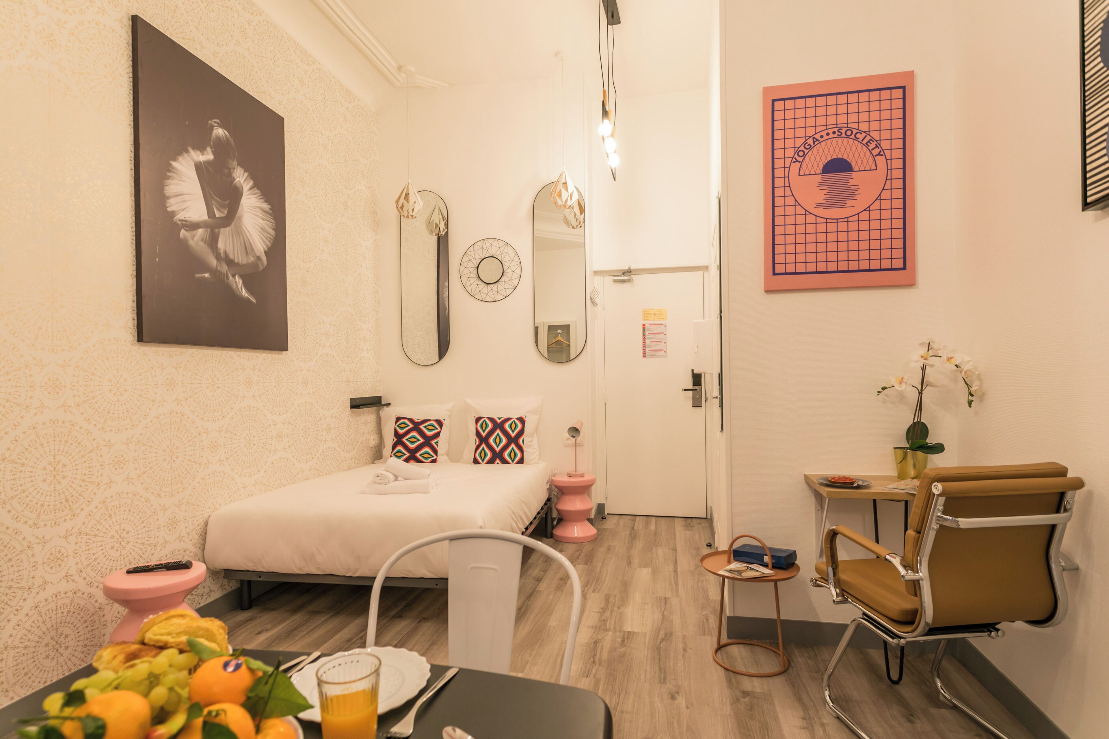 A modern hotel room with a bed, a desk, a chair, and a small table with fruit and a drink.