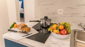 Une cuisine avec un plan de travail, une planche à découper avec du pain, un couteau, un saladier de fruits et une cuisinière.