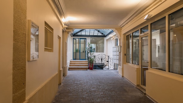Un couloir avec un sol en briques, une porte en verre au fond et une plante en pot.