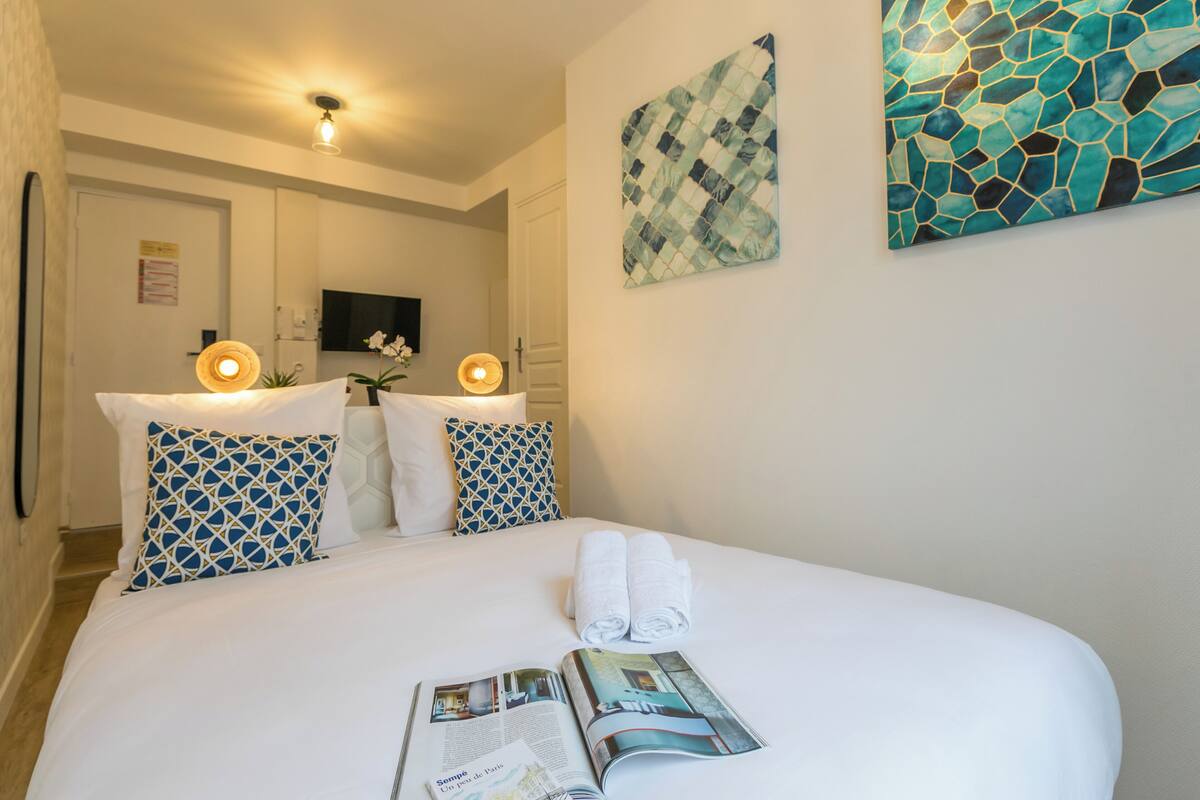 Un lit bien fait, avec des draps blancs, deux oreillers et deux serviettes enroulées. Un magazine est ouvert sur le lit.