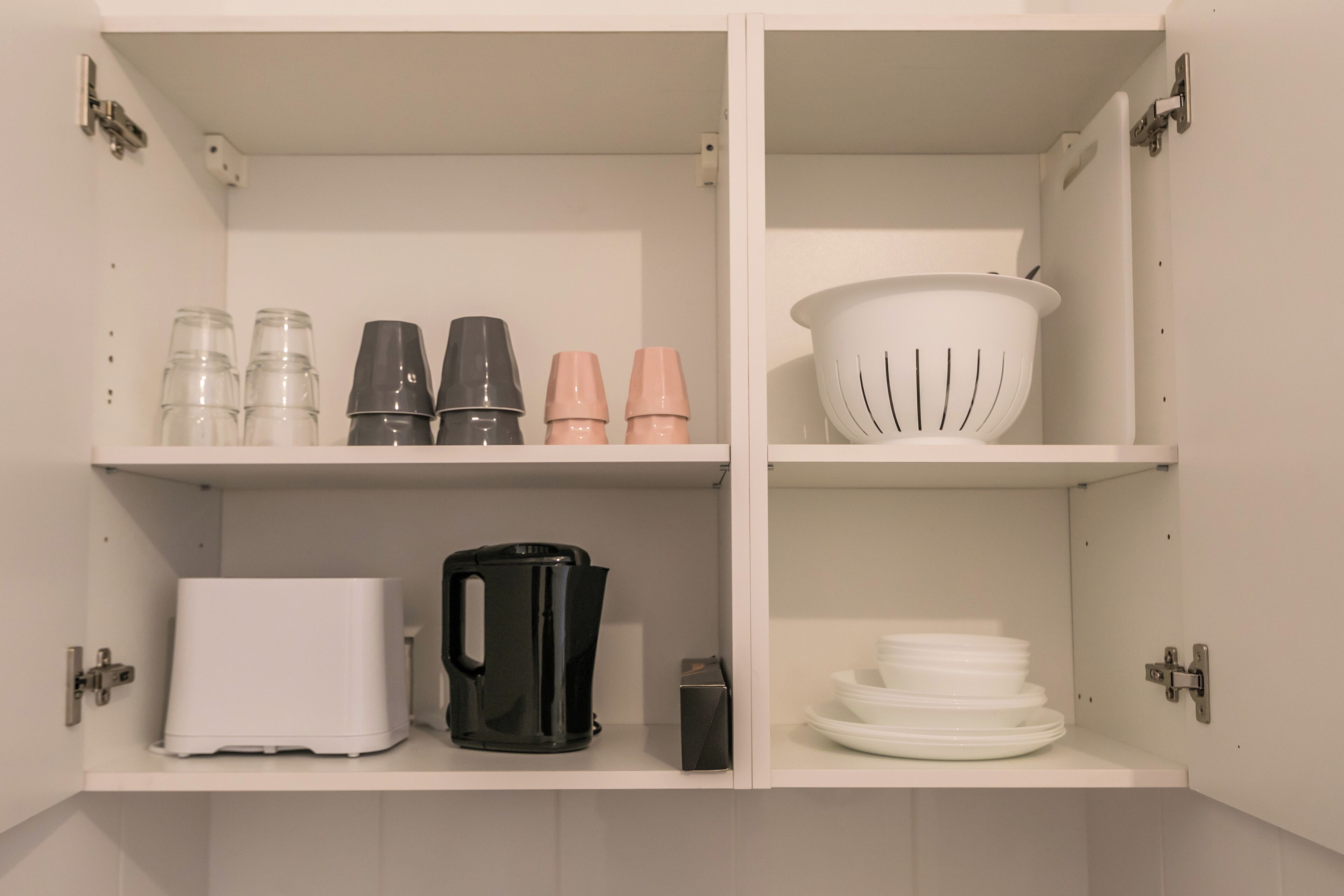 A kitchen with white cabinets, a toaster, a black coffee maker, and a colander on the upper shelf.