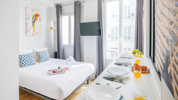Een hotelkamer met een bed, een televisie, een eettafel met borden en glazen, en een raam met gordijnen.