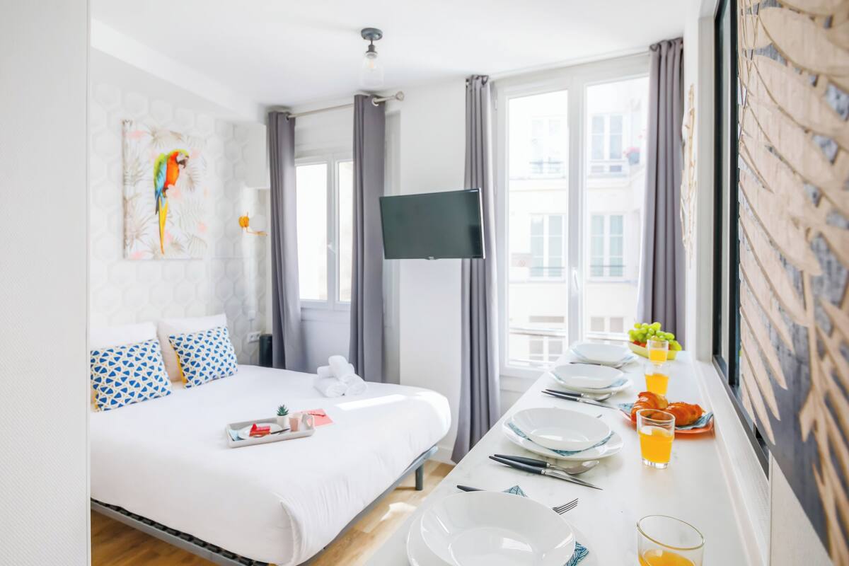 Une chambre d’hôtel avec un lit, une télévision, une table à manger avec des assiettes et des verres, et une fenêtre avec des rideaux.