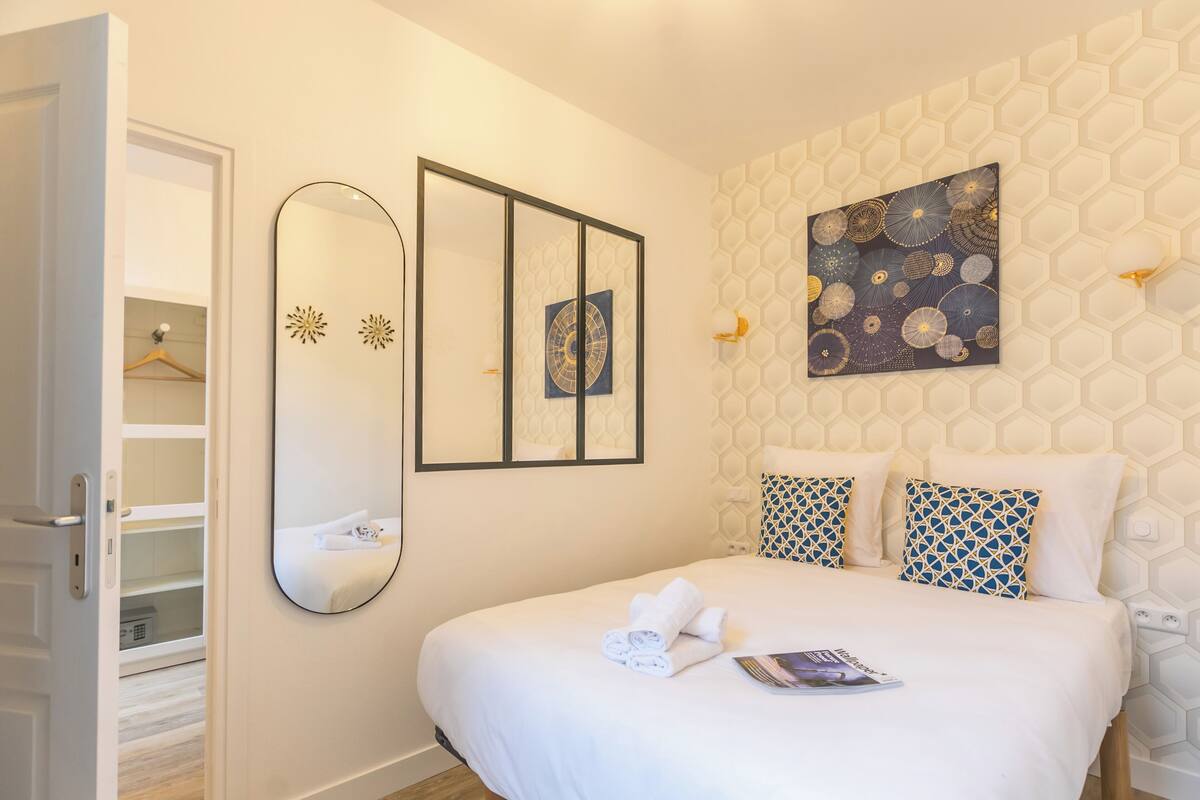 Une chambre d’hôtel avec un grand lit, une armoire, un miroir et un mur orné de motifs hexagonaux.