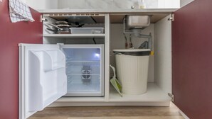 Een kleine keuken met een geïntegreerde koelkast, een gootsteen en een prullenbak.