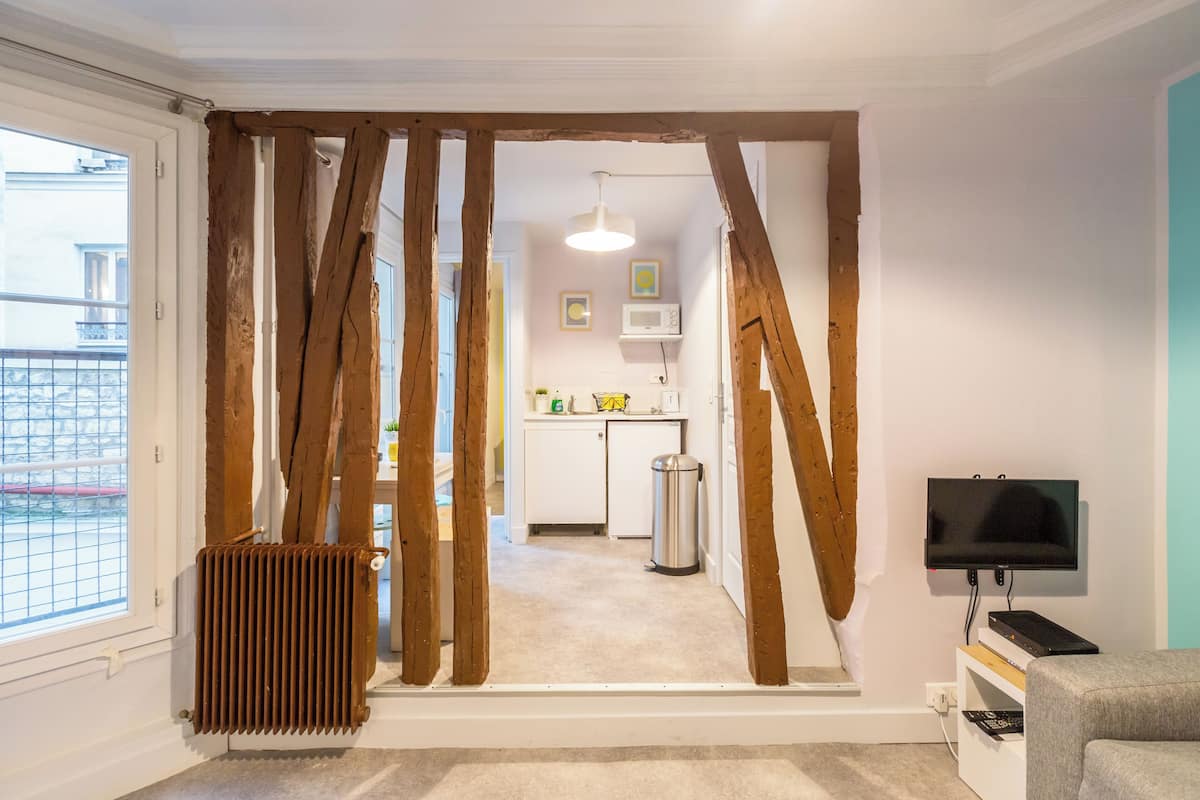 A modern apartment with exposed wooden beams, a kitchen with a microwave, and a TV in the living area.