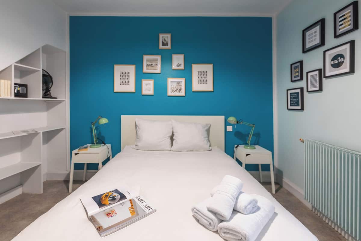 A hotel room with a large bed, white bedding, a blue accent wall, and several framed pictures.