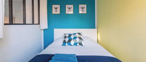 Un lit recouvert d’une couvre-lit bleue et blanche, un coussin à motifs géométriques et trois têtes d’animaux encadrées accrochées au mur.