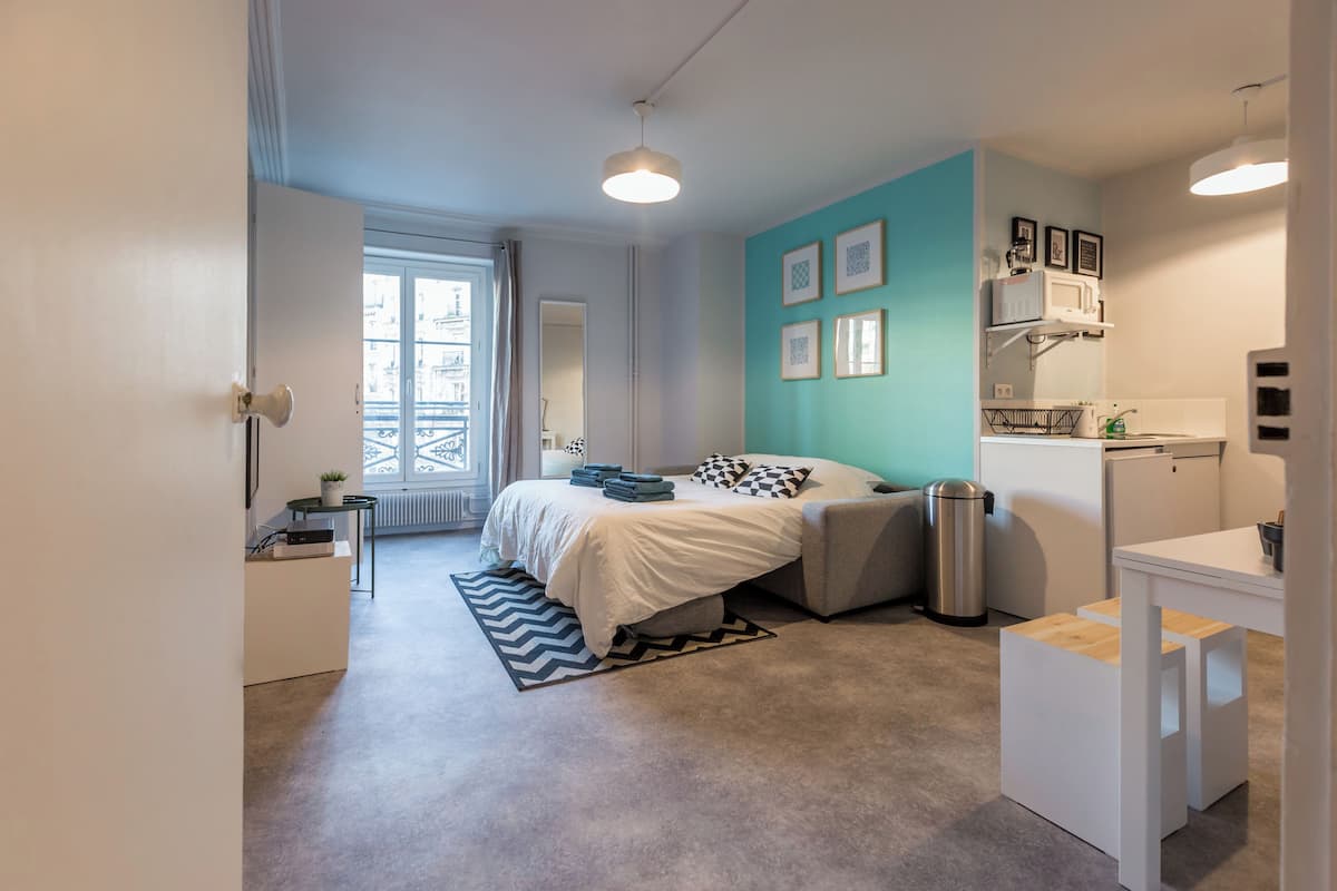 A modern bedroom with a bed, bedside tables, a small desk, a radiator, and a window.