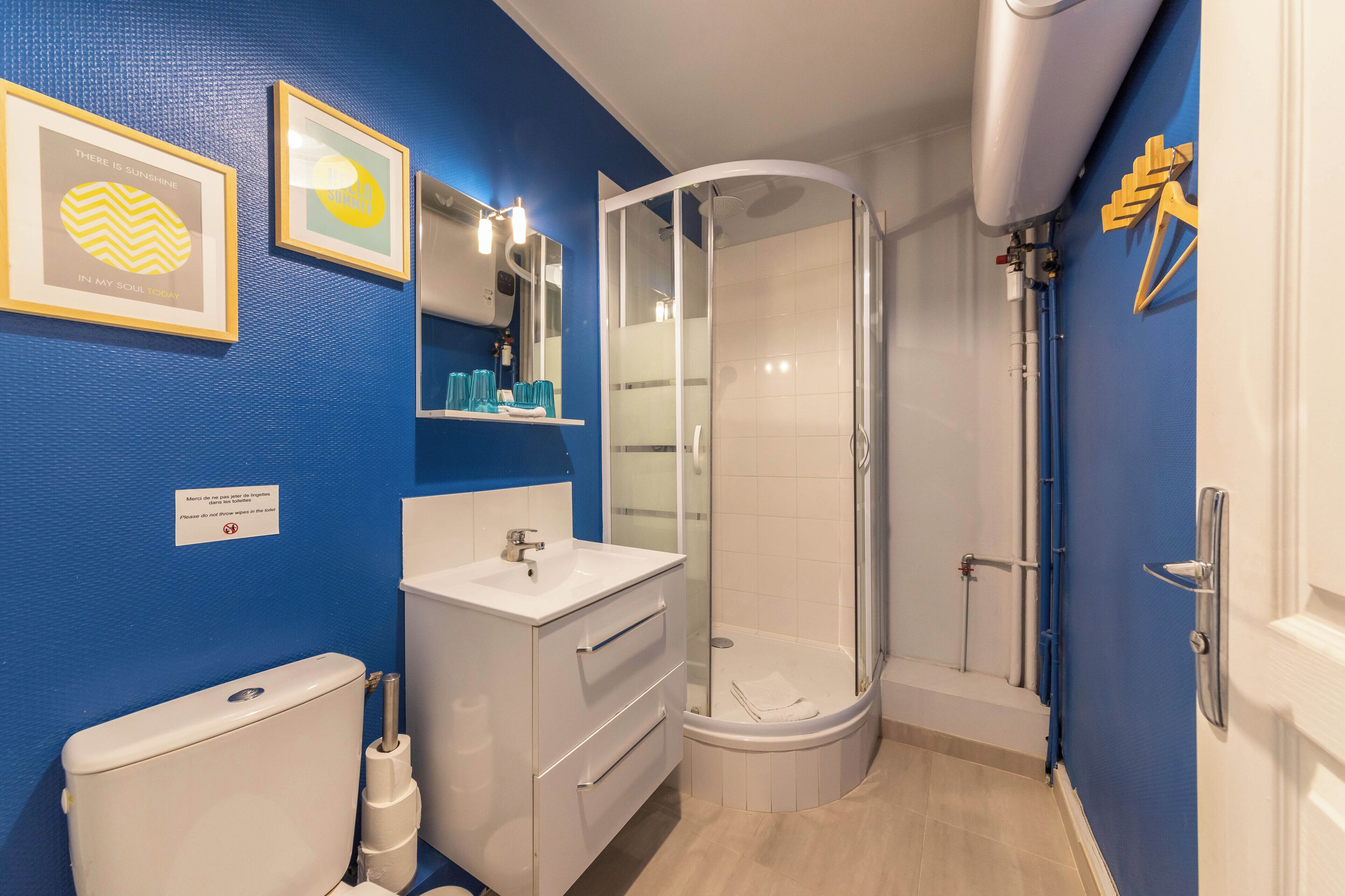 Un baño moderno con pared azul, lavamanos blanco, cabina de ducha con vidrio y retrete.