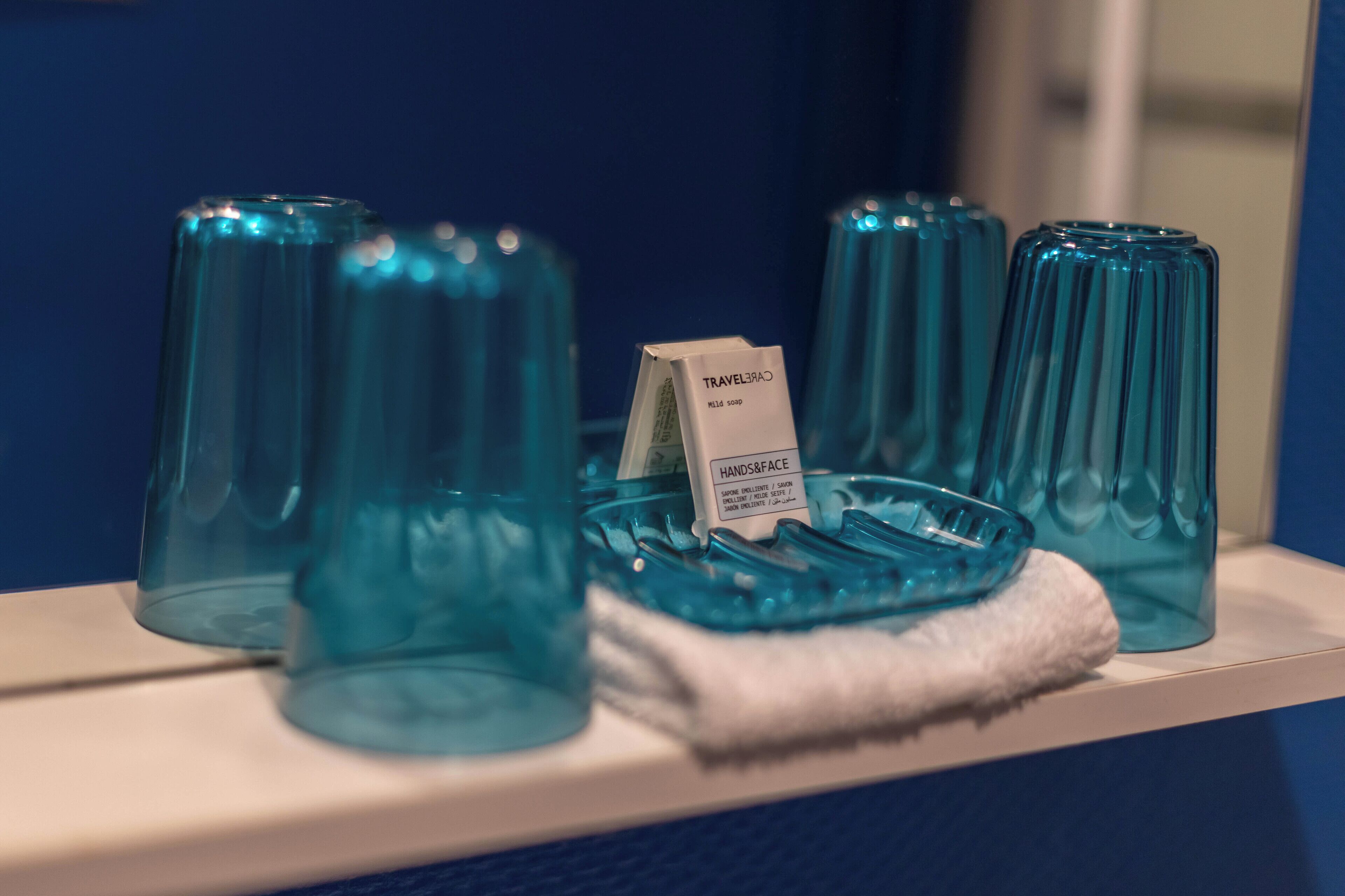 A display of blue glass containers on a shelf with a label reading "TRAVELER'S HANDS & FACE" and "MILK SOAP".