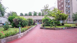 A pathway leading to a building with a red pavement, surrounded by greenery and flower beds. - WS Nation - Reuilly (Paris)