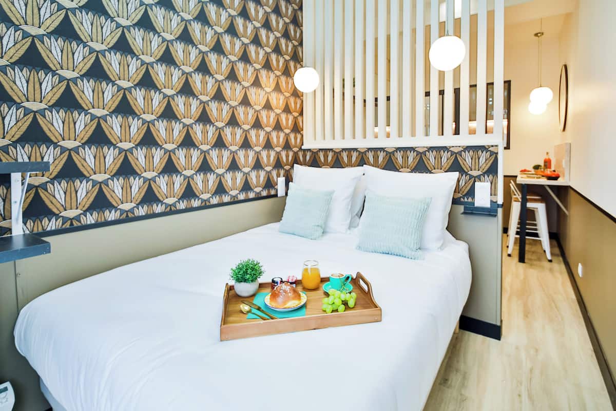 Una cama bien hecha con una bandeja de alimentos para el desayuno, una pared estampada y un diseño de habitación moderno.