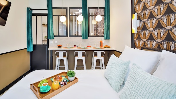 A hotel room with a bed, a breakfast tray, a small kitchen area with a bar, and a patterned wall. - WS Nation - Reuilly (Paris)