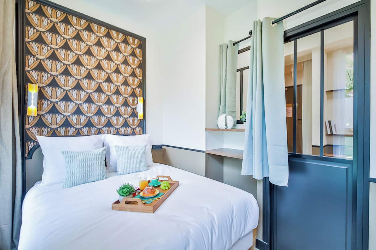 Habitación de hotel con una cama, una bandeja con alimentos para el desayuno, un cabecero con diseño y vistas a través de una puerta corrediza.