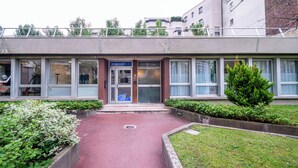 A building with a red pathway leading to a glass door entrance, surrounded by greenery and a small tree. - WS Nation - Reuilly (Paris)