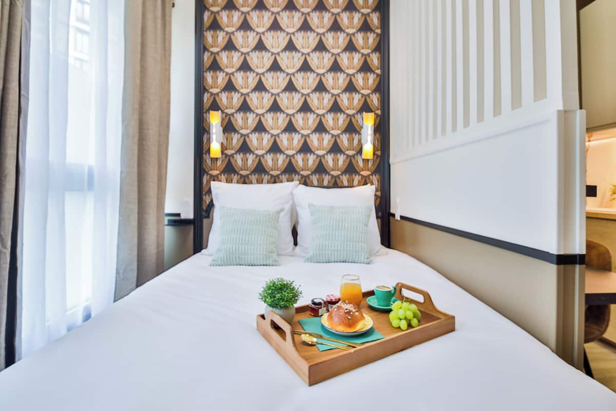Una habitación de hotel con cama, una bandeja con alimentos para el desayuno y una pared con diseño.