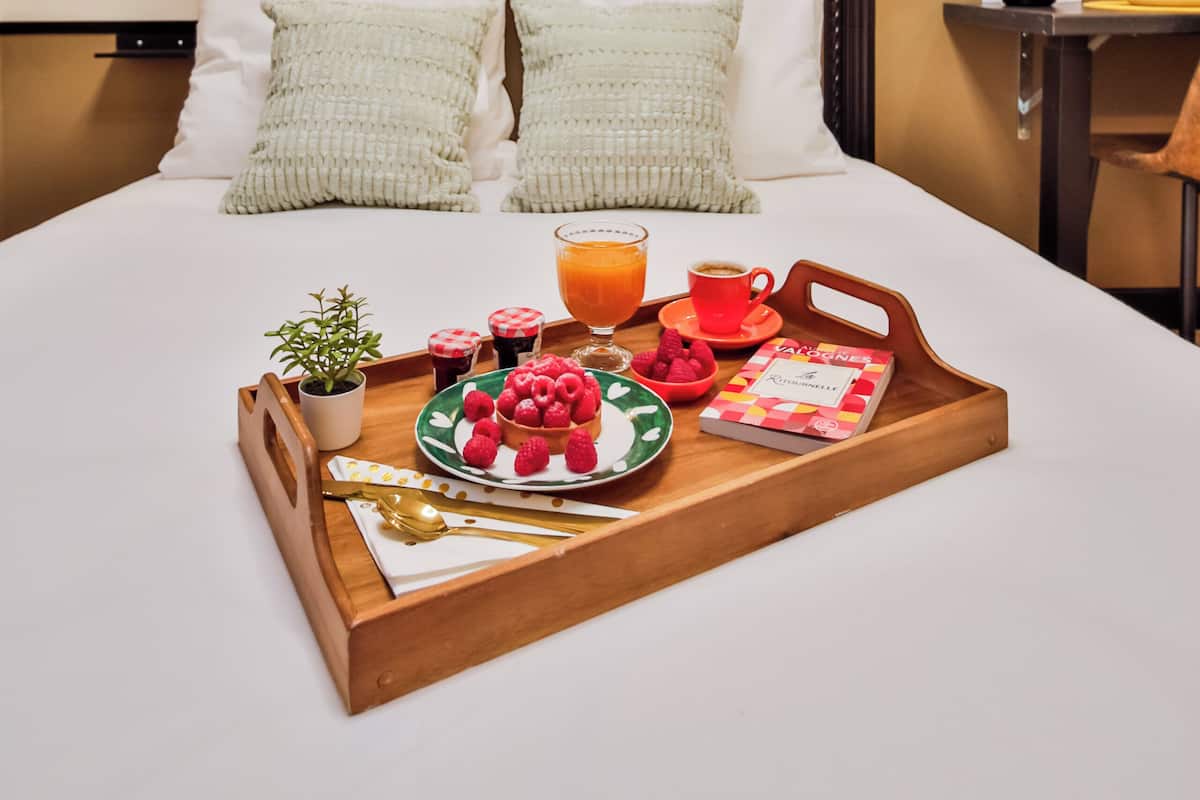 A neatly made bed with a tray of breakfast items including fruit, a drink, and a book.
