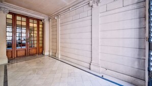 Un vestíbulo amplio con piso de baldosas, una puerta de madera grande con paneles de vidrio y una pared lisa con molduras decorativas.