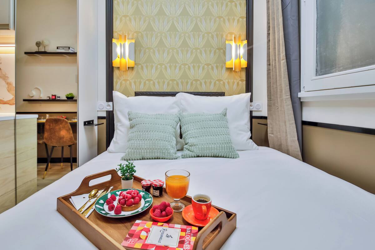 A neatly made bed with a tray of breakfast including raspberries, a glass of orange juice, and a cup of coffee.