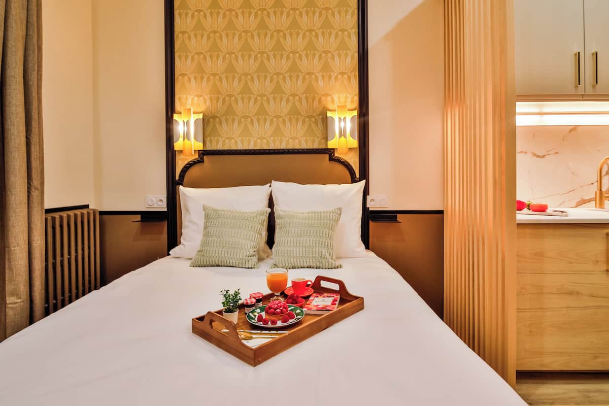 A neatly made bed with a tray of breakfast items, including a plate of fruit, a cup of coffee, and a glass of orange juice.