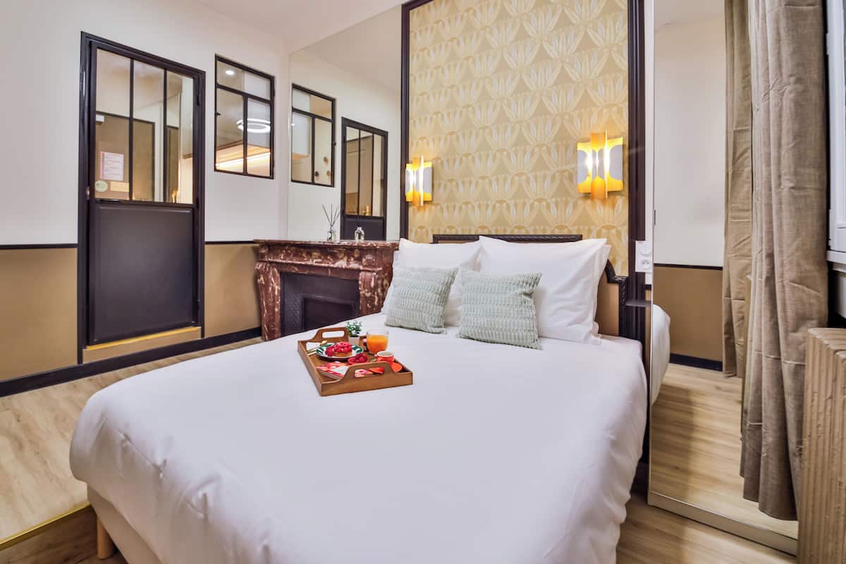 A hotel room with a large bed, a fireplace, and a breakfast tray on the bed.