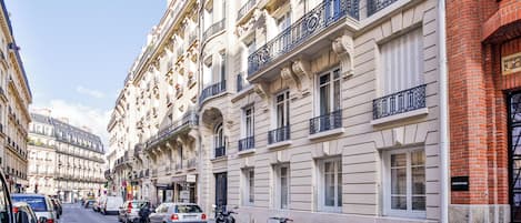 A street view of a row of classic European-style buildings with balconies, parked cars, and bicycles.