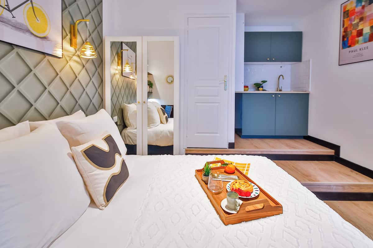 A hotel room with a bed, a tray with breakfast items, a kitchen area, and a door leading to another room.