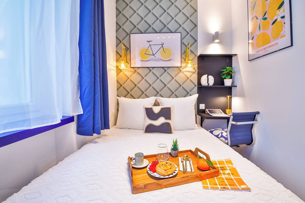 A neatly arranged hotel room with a bed, a bedside table with a lamp, a small desk, and a chair.