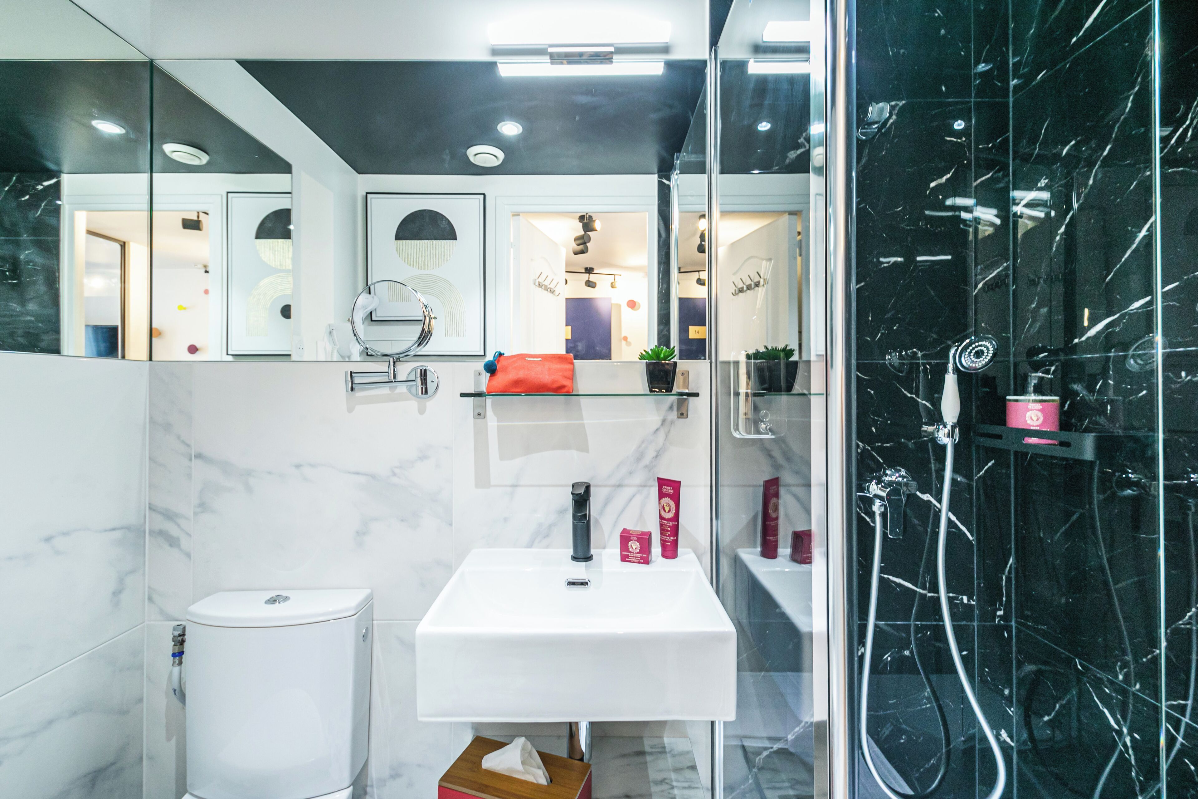 A modern bathroom with a white sink, black marble walls, and a glass shower enclosure.
