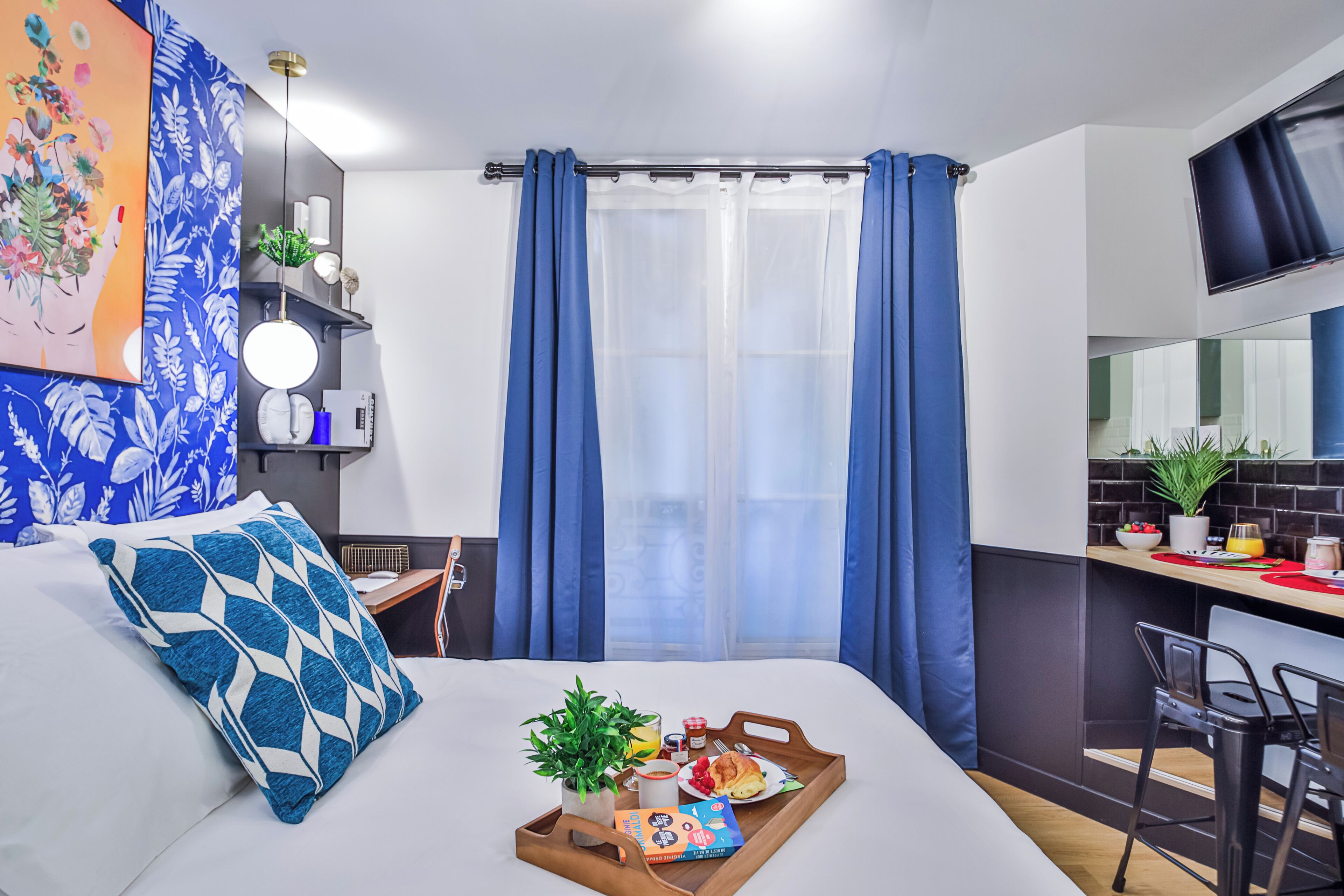 A modern hotel room with a bed, a breakfast tray, a desk, and a TV.