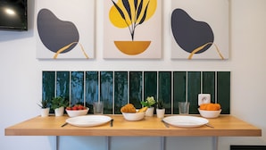 Una mesa de comedor con platos, tazones y cubiertos, frente a una pared decorada con arte abstracto y un salpicadero de azulejos verdes.