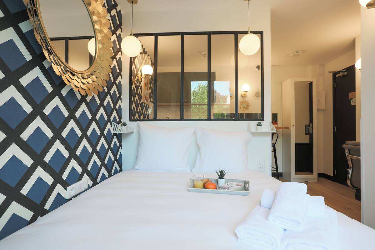 A neatly made bed with white linens, a tray with fruits and a plant, and a geometric patterned wall.
