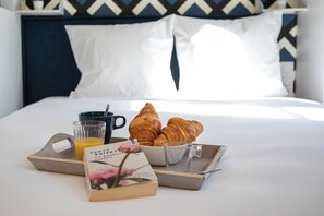 A neatly made breakfast tray with croissants, a glass of orange juice, and a book on a bed with white bedding and a patterned headboard. - WS Notre-Dame - Linné (Paris)