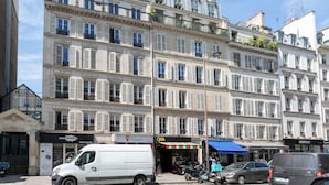 Un edificio de varios pisos con un estilo arquitectónico europeo clásico, que cuenta con balcones con plantas y diversas tiendas en la planta baja.