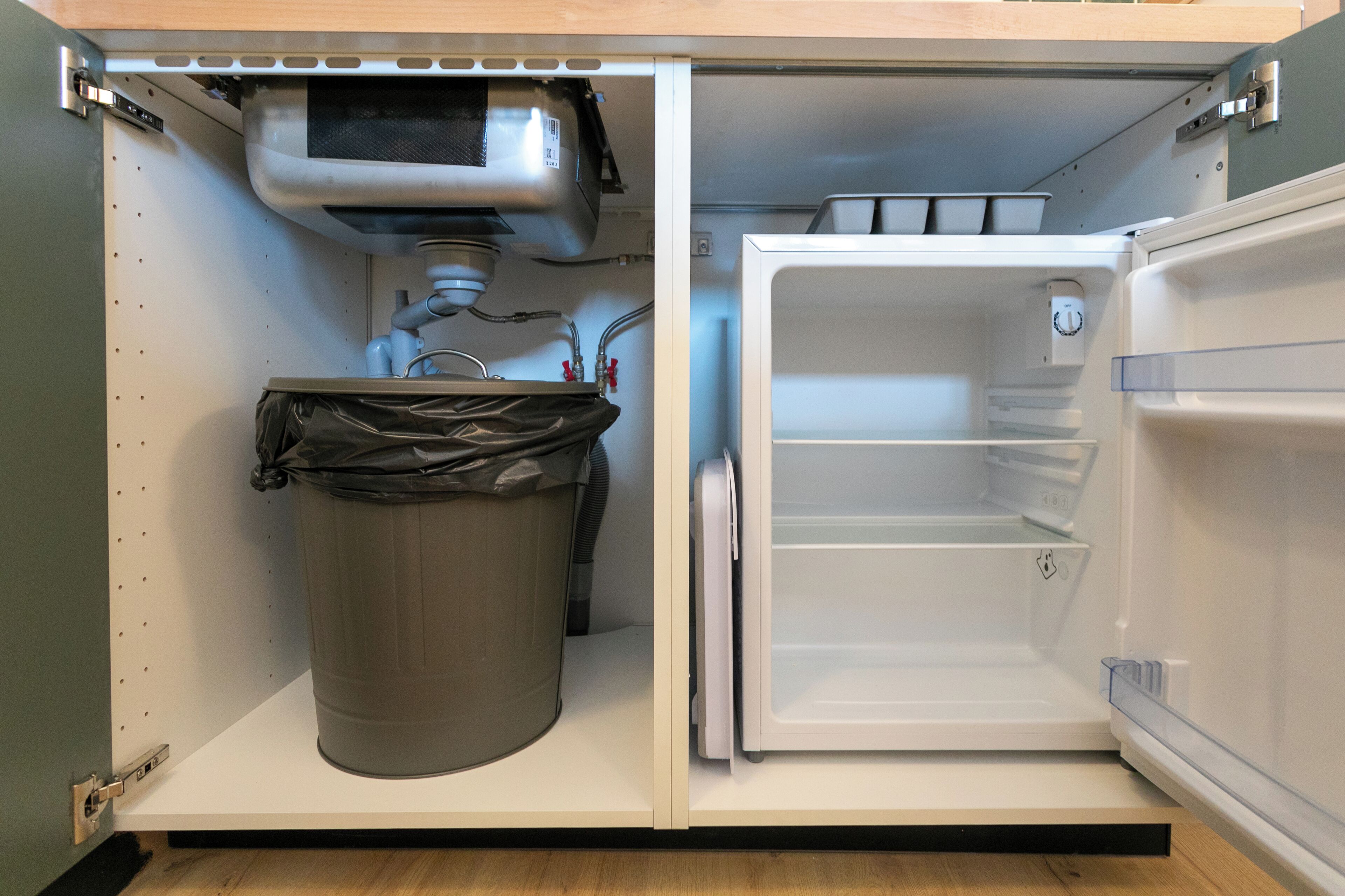 A compact kitchen with a built-in refrigerator, a trash bin, and a small countertop.