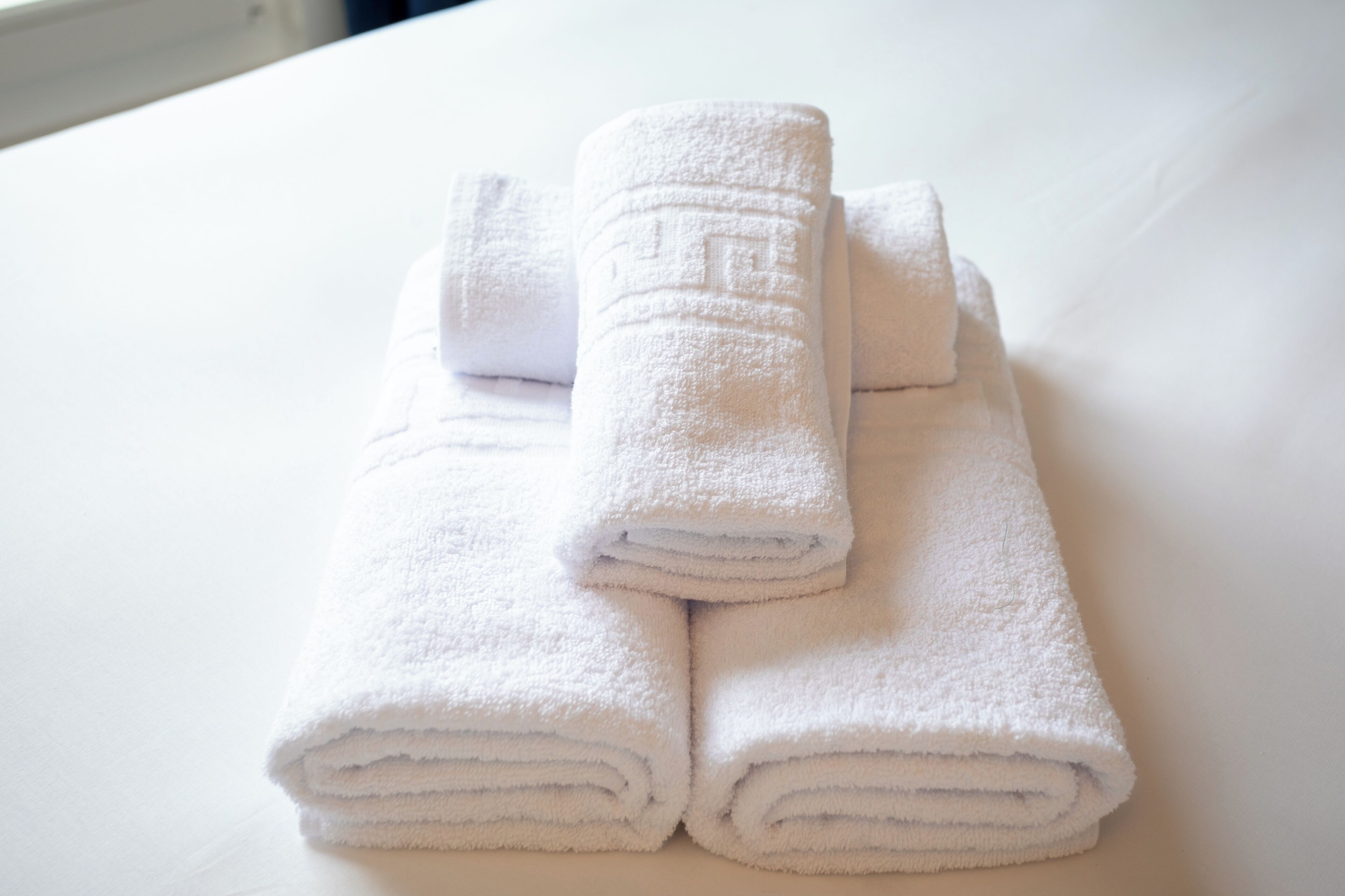 Three neatly folded white towels stacked on a white surface.