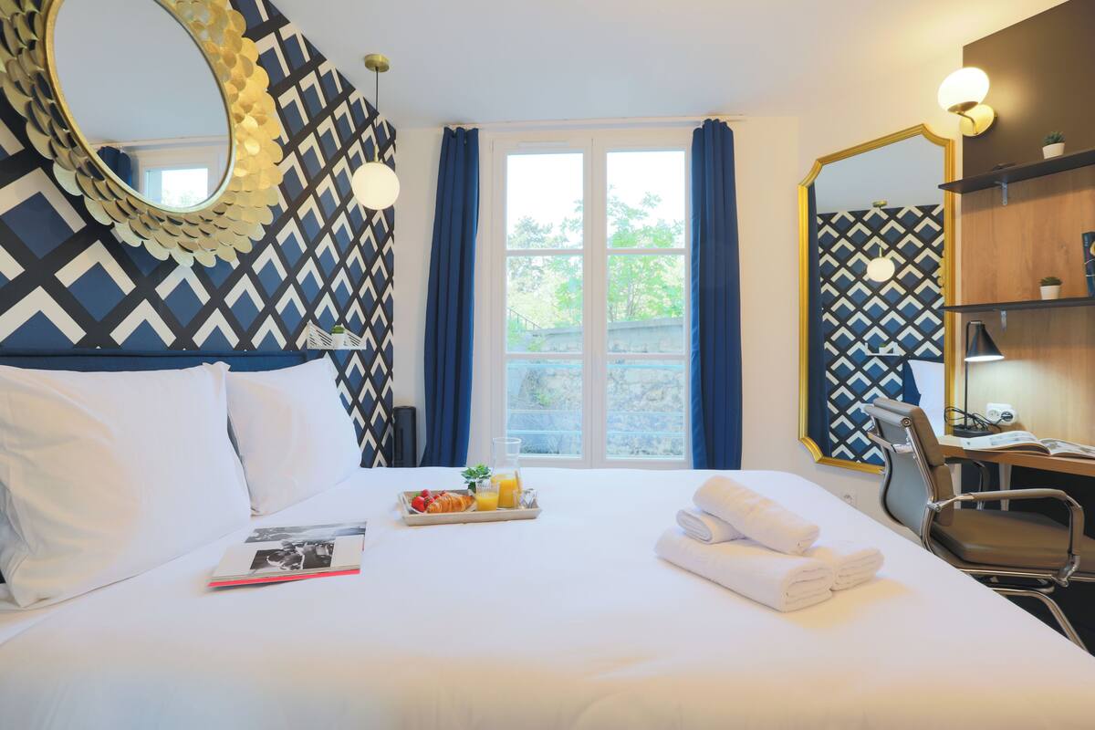 A hotel room with a bed, a breakfast tray, a mirror, and a desk with a chair.