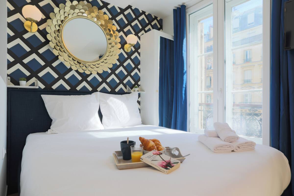A neatly made bed with white linens, a tray with croissants and orange juice, and a book on the side.