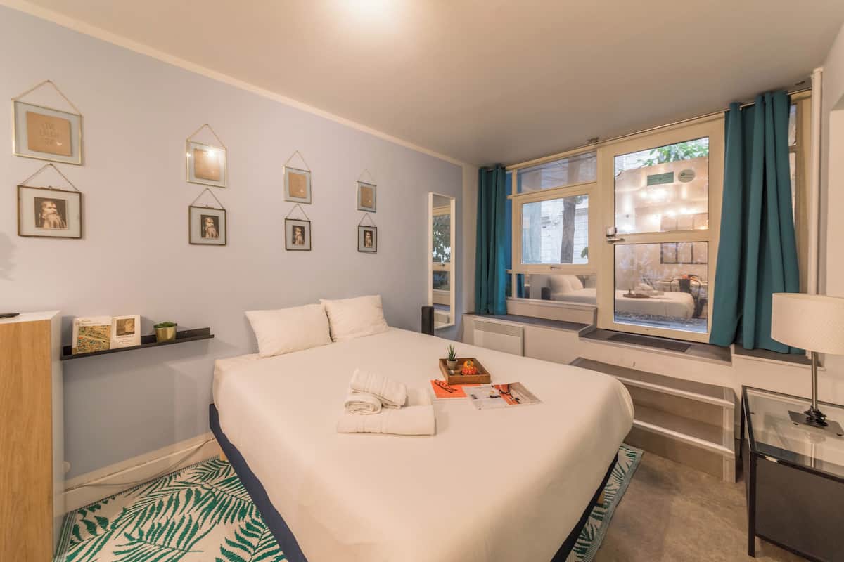 A hotel room with a large bed, a window with curtains, a bedside table with a lamp, and wall-mounted pictures.