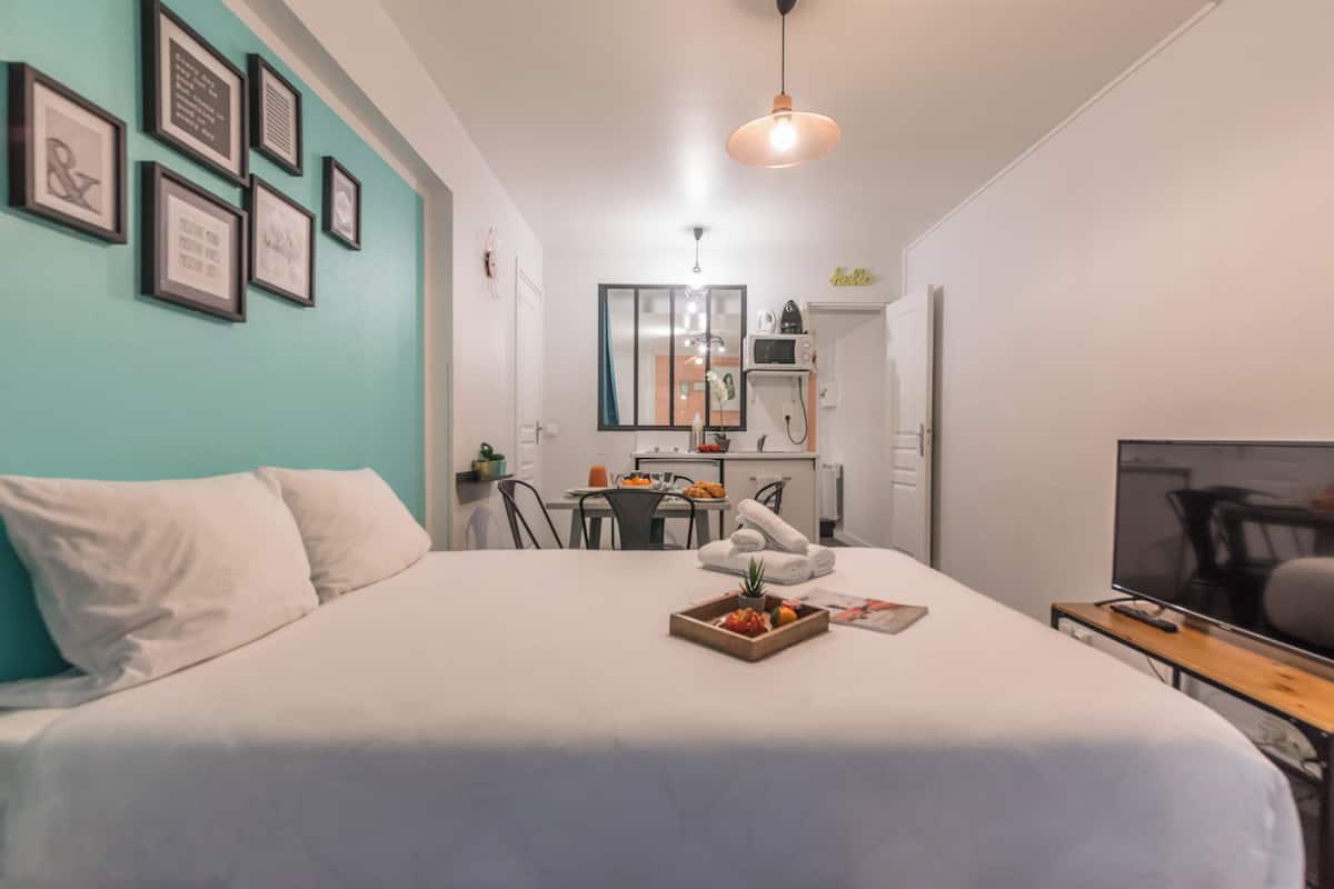 A hotel room with a bed, a desk, a TV, and a kitchenette.