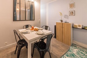 A dining area with a white table, black chairs, and a wooden cabinet. - (Paris)