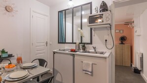 A compact kitchen with a microwave, sink, and small refrigerator. There is a dining table with plates and a bowl of fruit. - WS Montmartre - Sacré Coeur (Paris)
