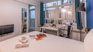 A hotel room with a bed, a TV, a dining table with chairs, a window with curtains, and a plant. - WS Montmartre - Sacré Coeur (Paris)