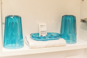 A bathroom shelf with a blue glass soap dish, a white soap bar, and a white towel. - (Paris)
